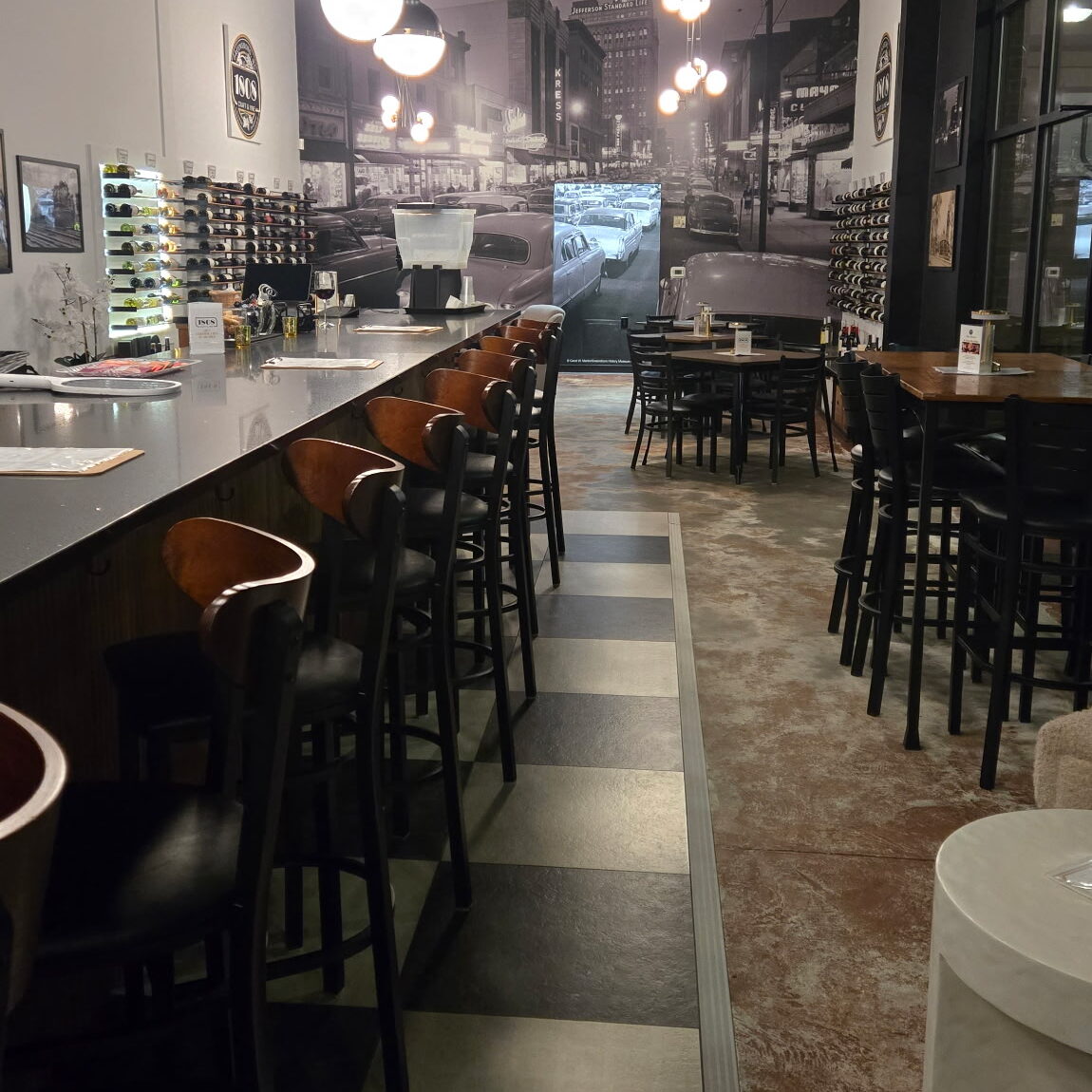 Image of an empty bar with checkered flooring and black furniture.