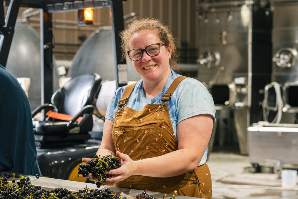 Person standing in front of conveyor belt smiling with grapes in hand.
