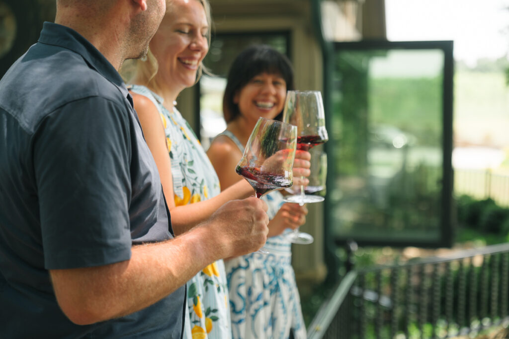 Three people enjoying wine on a balcony.